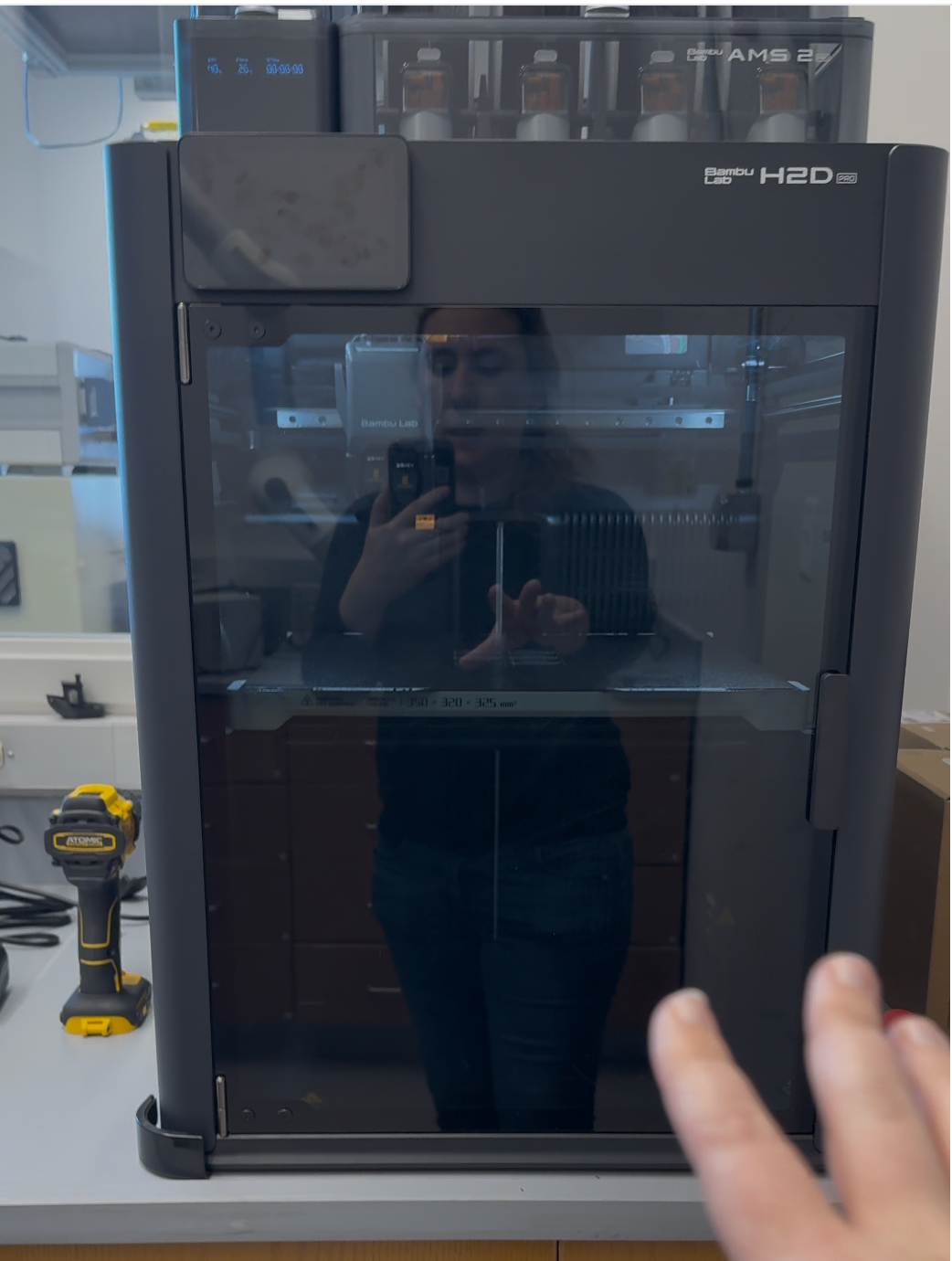 Photograph of an enclosed Bambu Lab 3D printer with a glass front door on a laboratory bench.