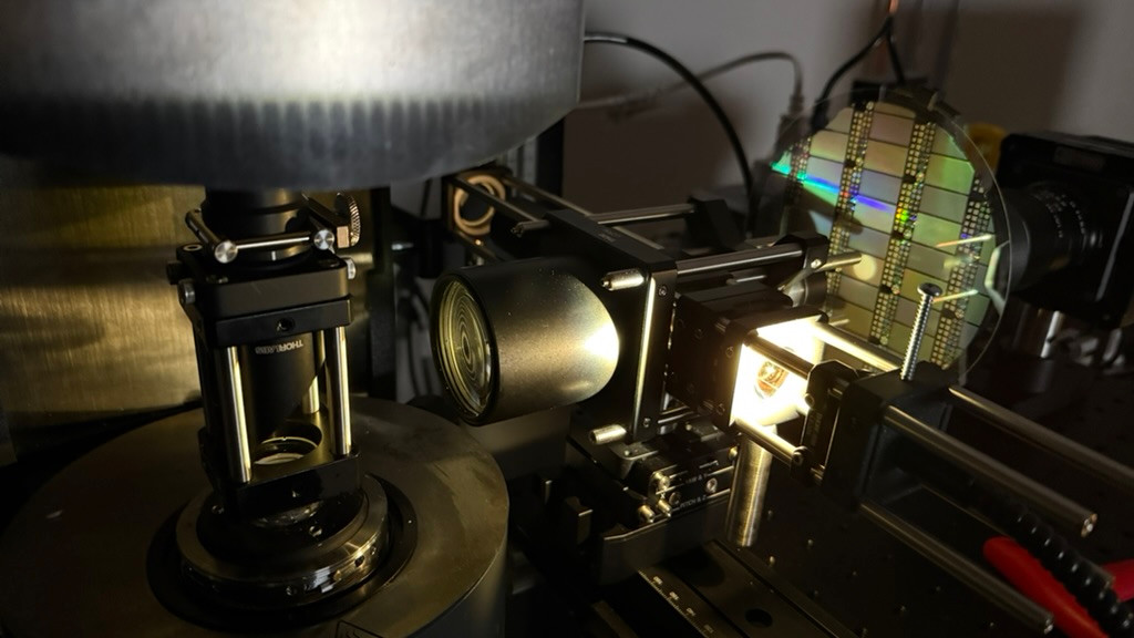 An optical apparatus with a transparent vertical cylinder, lenses and mounts, a bright illuminated region, and a circular reflective element.